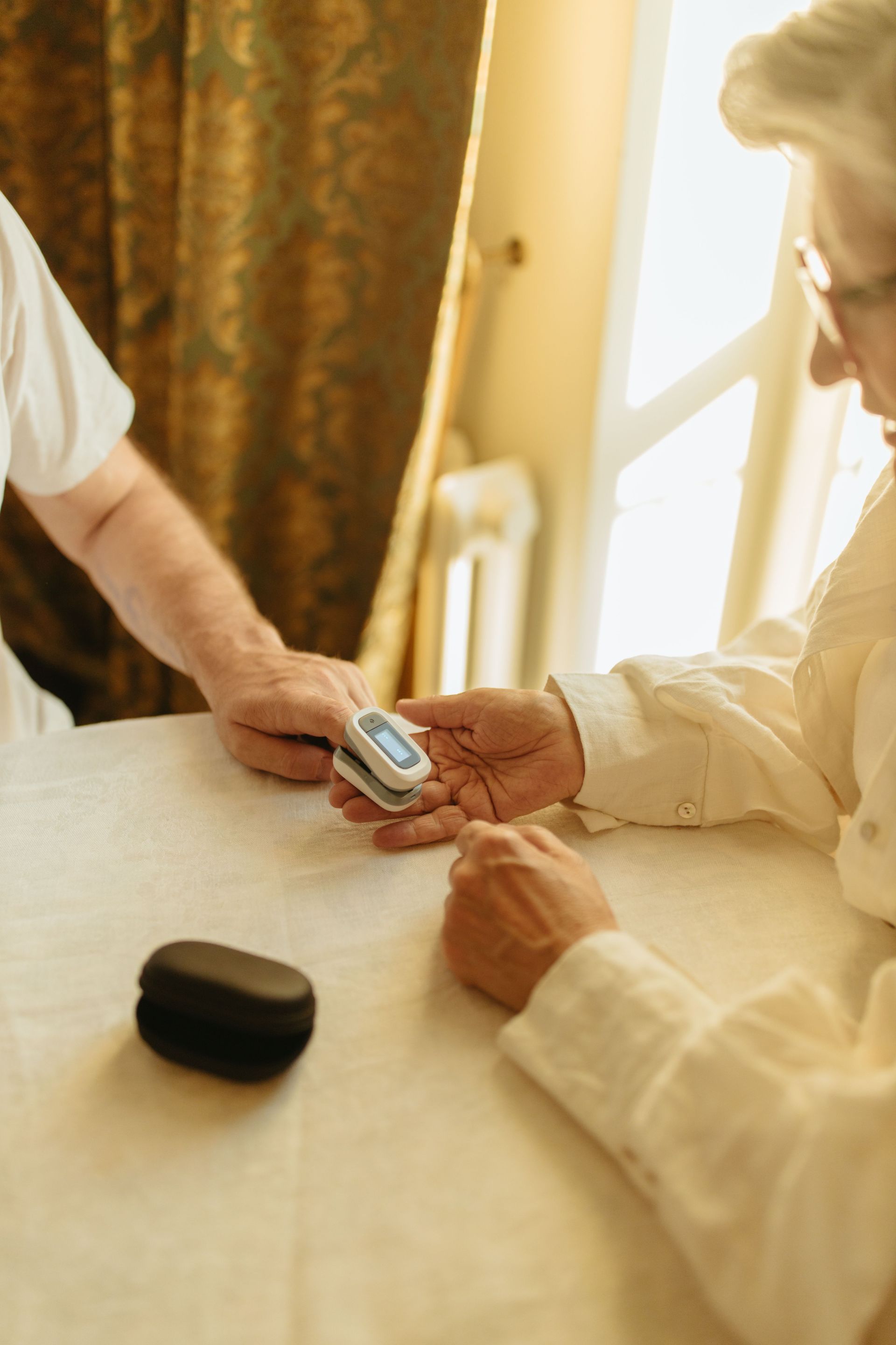 Elderly person using a pulse oximeter indoors for health monitoring.