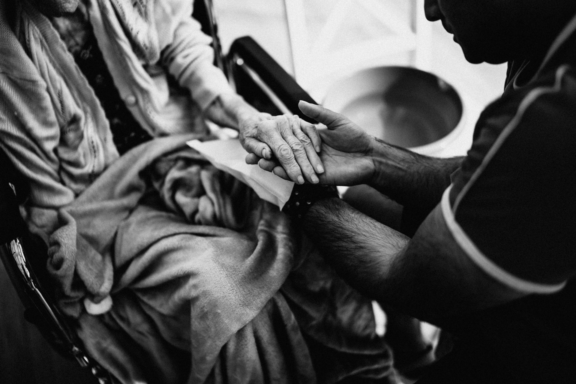 A caregiver holding the hands of an elderly woman in a wheelchair, emphasizing empathy and support.