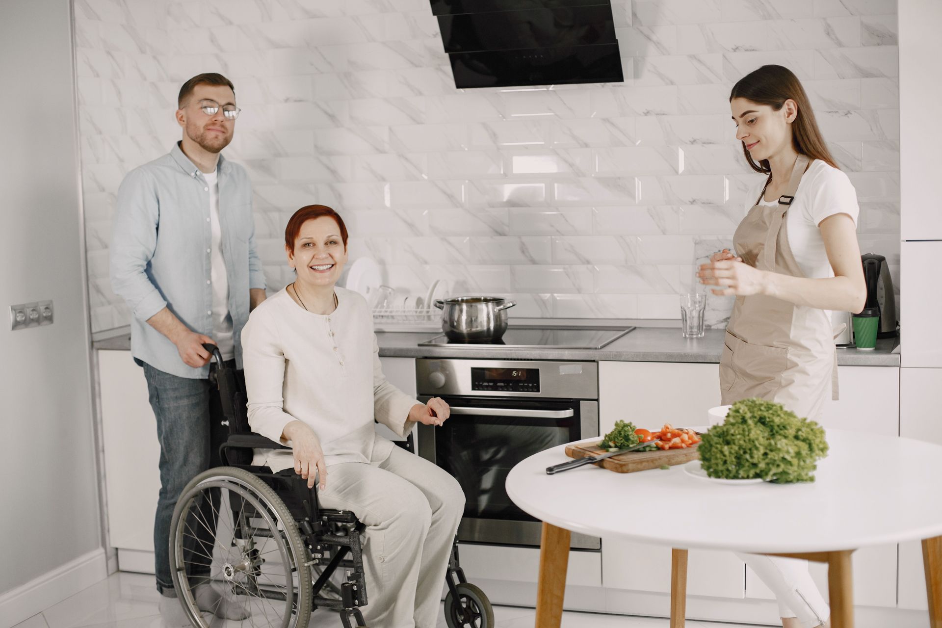 Three adults enjoying family time preparing food in a bright kitchen.